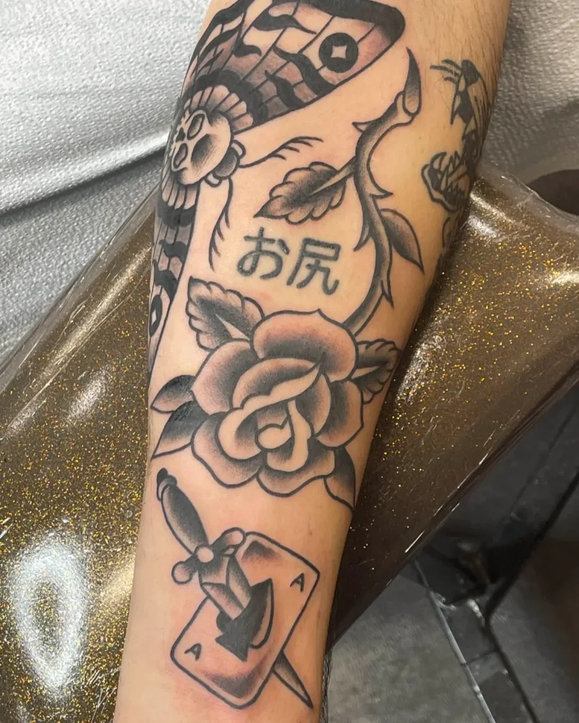 Black and grey rose tattoo with script and traditional elements on forearm