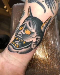 Traditional Japanese oni mask tattoo with yellow eyes on forearm